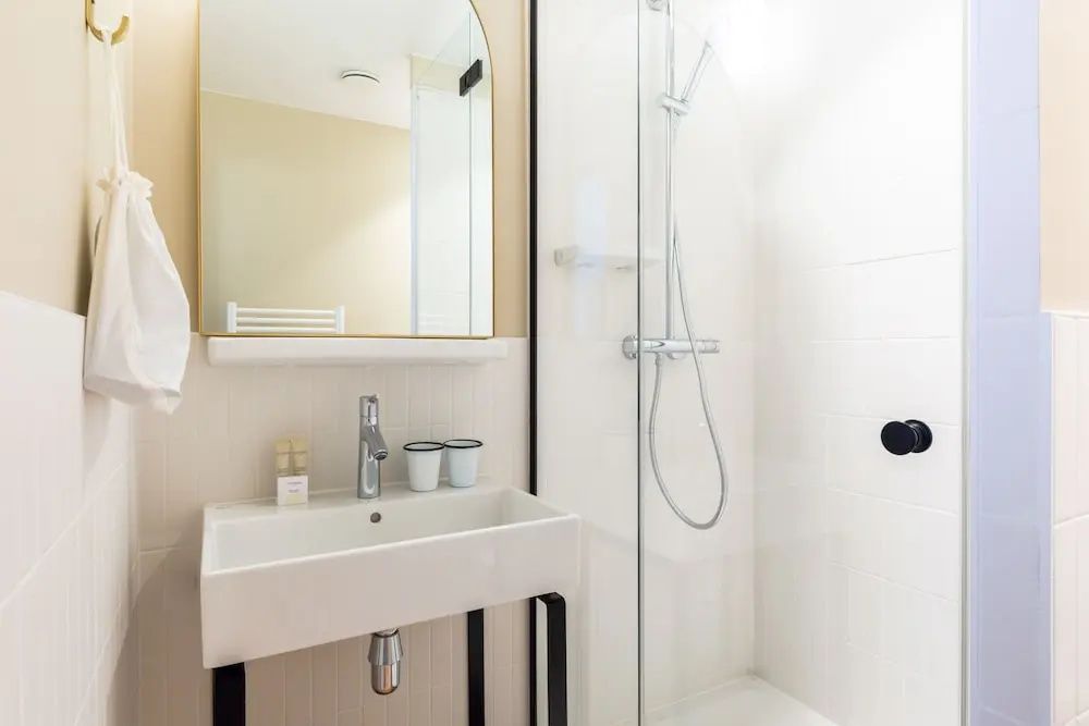 Badezimmer mit weißem Waschbecken, rechteckigem Spiegel und bodengleicher Glasdusche.