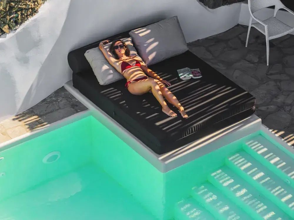 Frau liegt auf einer Liege neben einem beleuchteten türkisfarbenen Pool.