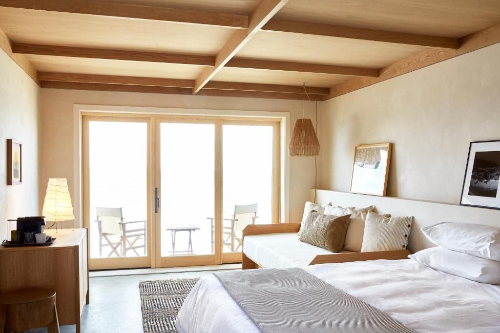 Geräumiges Zimmer mit Holzbalkendecke, Sitzgelegenheit und großer Glasfront zur eigenen Terrasse.