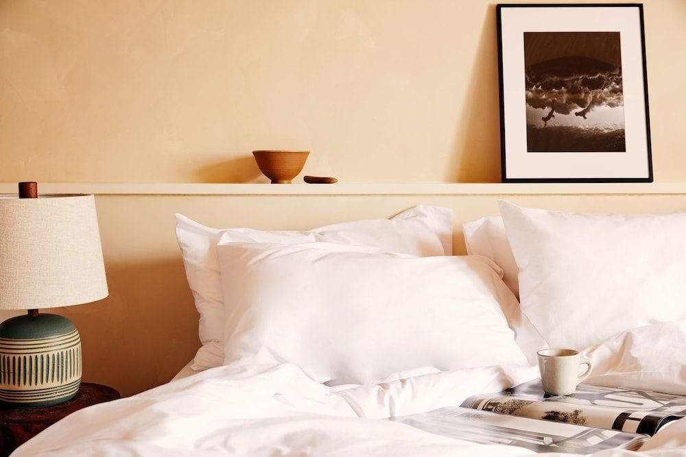 Bett mit weißen Kissen, aufgeschlagenem Magazin und Kaffeetasse.