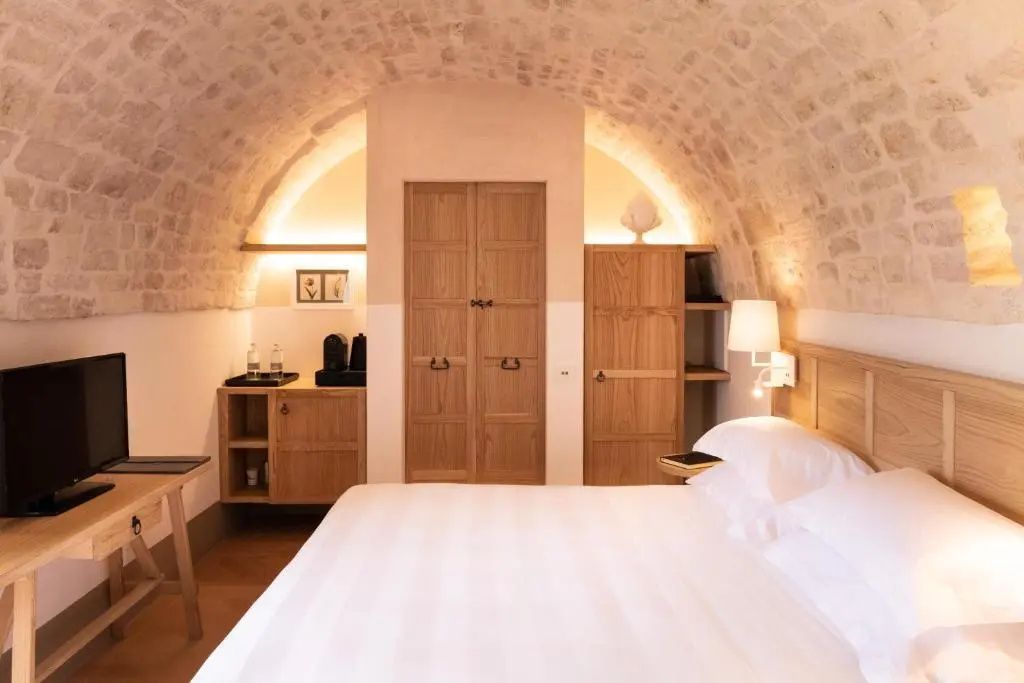 Hotelzimmer mit gewölbter Steindecke, weiß bezogenem Bett und warmen Holzmöbeln.