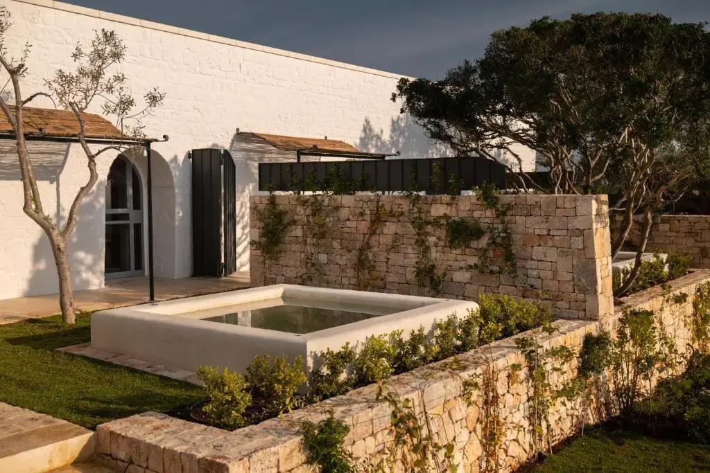 Kleines Wasserbecken auf einer Terrasse mit Natursteinmauern und weißer Gebäudewand.