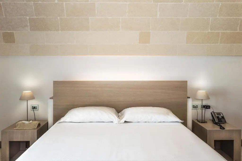 Doppelbett mit weißer Bettwäsche vor einer Wand aus hellen Steinquadern.