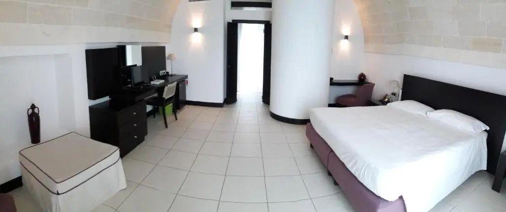 Helles Hotelzimmer mit großem Doppelbett, Schreibtisch und weiß gestrichenen Wänden.