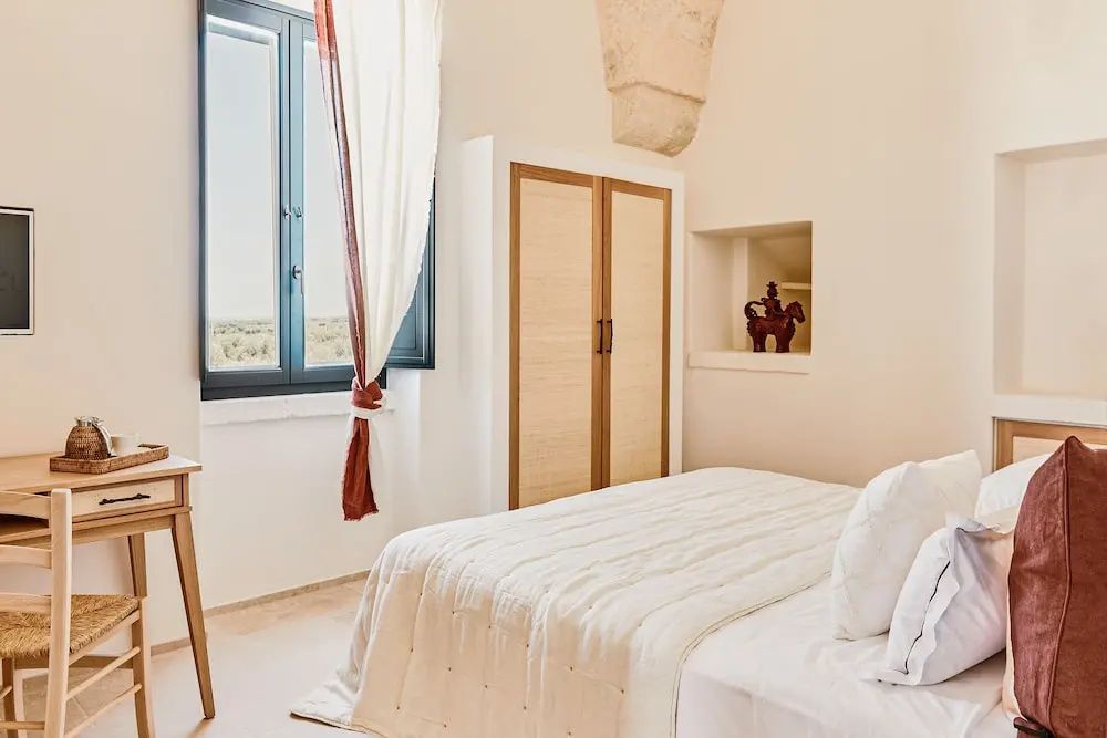 Helles Hotelzimmer mit Doppelbett, weißer Bettwäsche, Holzschrank und hohem Fenster.