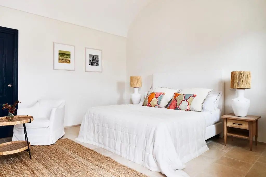 Helles Hotelzimmer mit weiß bezogenem Doppelbett, bunten Kissen und Sessel
