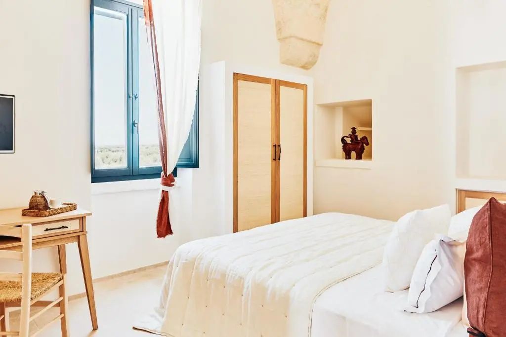Helles Hotelzimmer mit Doppelbett, Holzkleiderschrank und blauem Fensterrahmen.