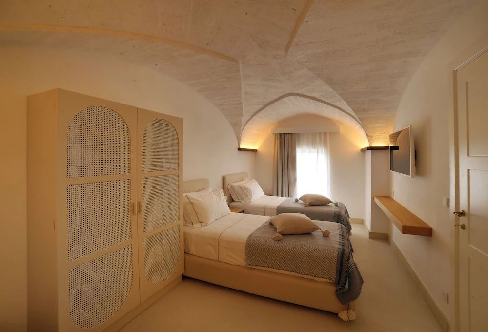 Hotelzimmer unter einer historischen Gewölbedecke mit zwei Einzelbetten und hellem Schrank.