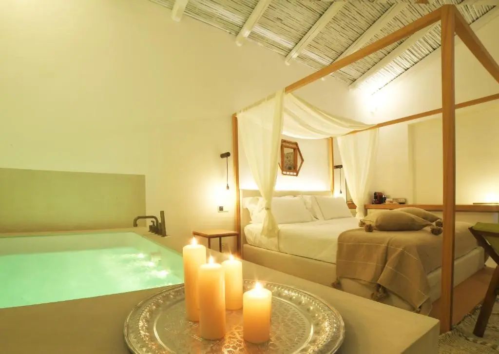 Schlafzimmer mit Himmelbett, brennenden Kerzen auf einem Tablett und kleinem Innenpool unter hellem Dach.