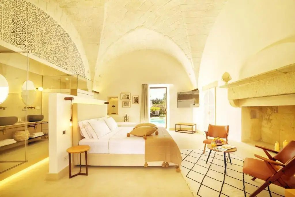 Hell eingerichtetes Zimmer mit Gewölbedecke, Doppelbett, Sitzgelegenheiten und Blick zum Außenbereich.
