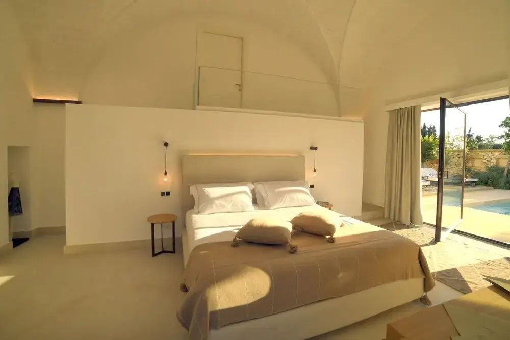 Schlafzimmer mit großem Doppelbett, beigefarbener Tagesdecke und hellem Gewölbe.