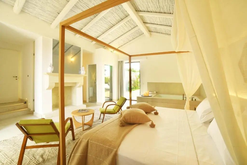 Helles Schlafzimmer mit großem Himmelbett, Holzmöbeln und zwei grünen Sesseln.
