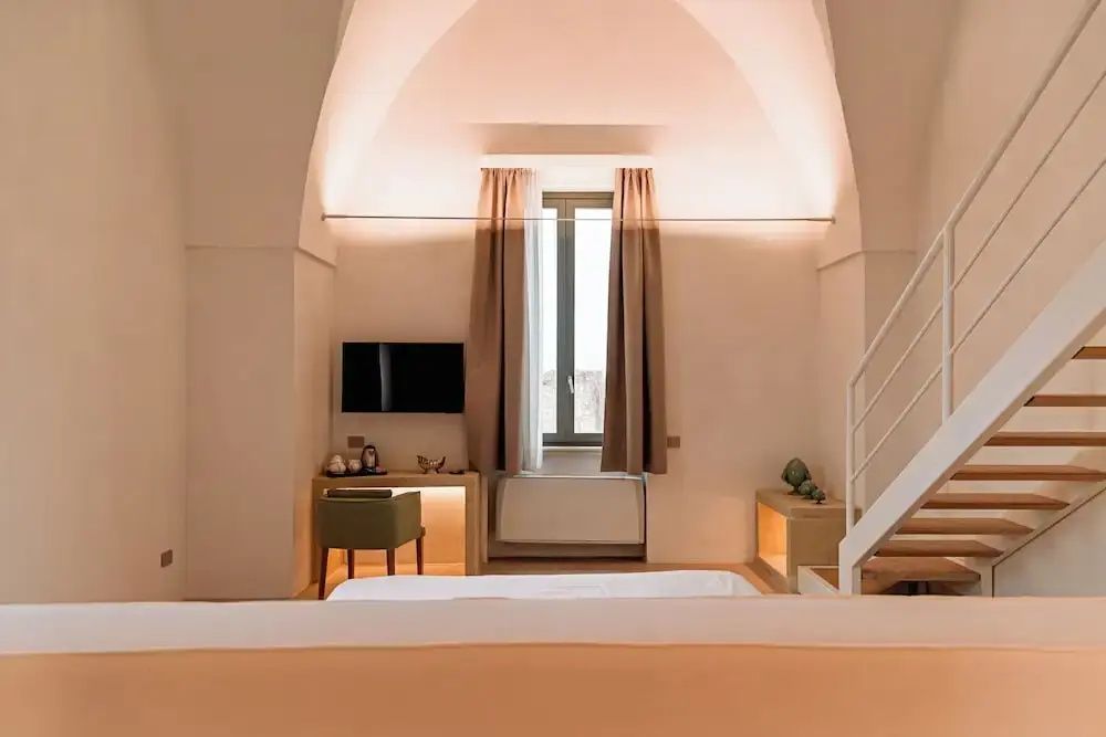 Schlafzimmer mit gewölbter Decke, Fenster, Wandfernseher und Schreibtisch sowie Bett im Vordergrund.