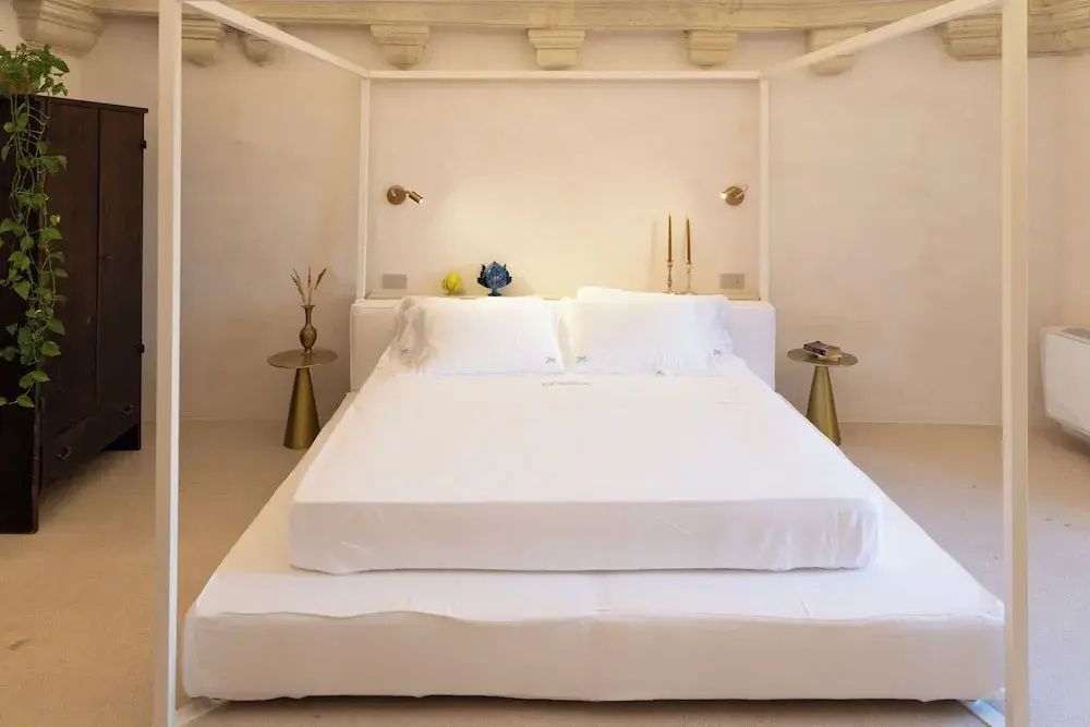 Weiß gemachtes Himmelbett in einem hellen Zimmer mit kleinen metallischen Beistelltischen.