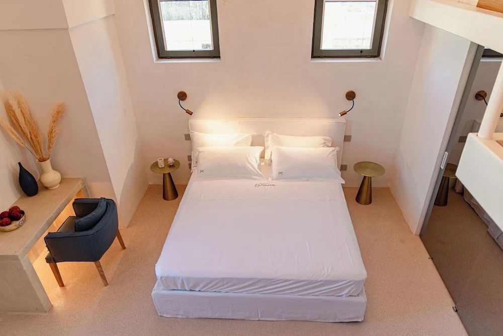Doppelbett mit weißer Bettwäsche, zwei Nachttischen und kleinen Fenstern darüber.