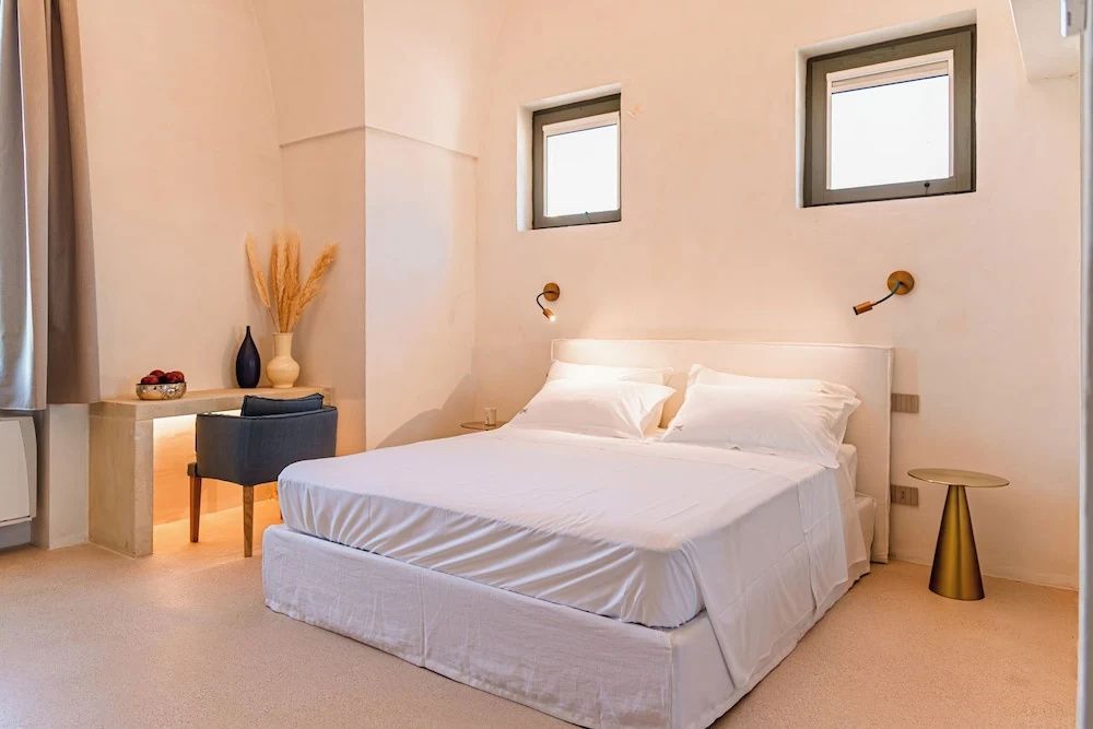 Weißes Doppelbett in einem hell gestalteten Schlafzimmer mit kleinem Schreibtisch.
