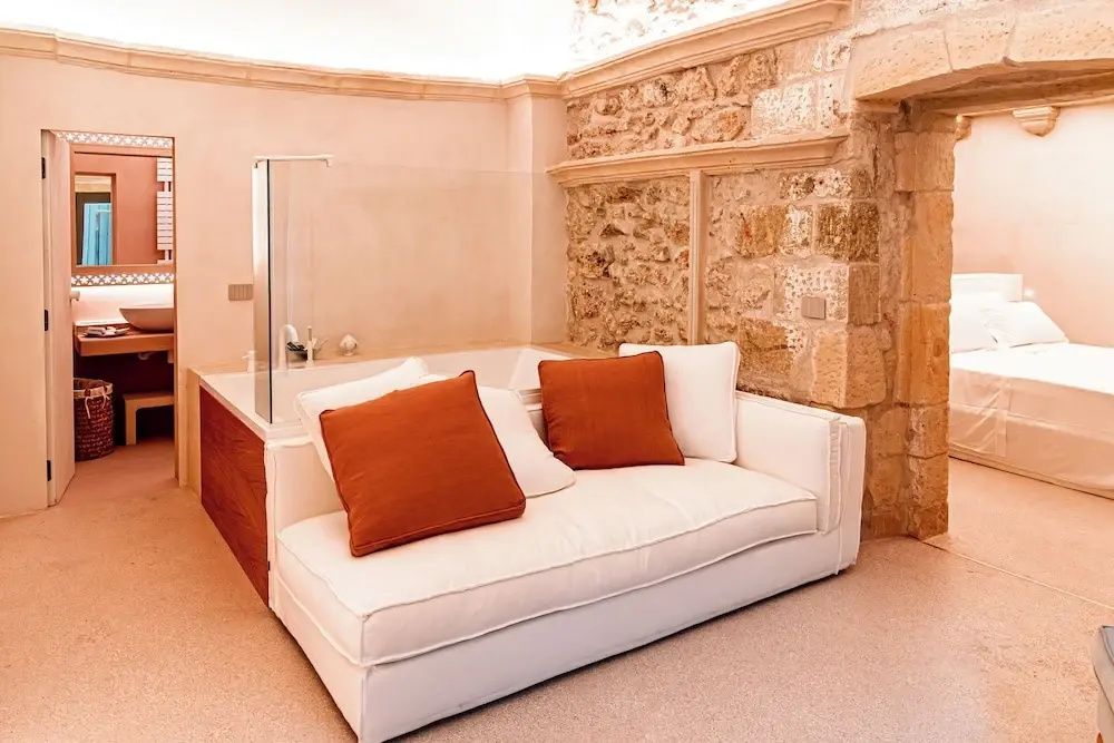 Weißes Sofa mit orangefarbenen Kissen vor einer Wand aus hellem Naturstein.