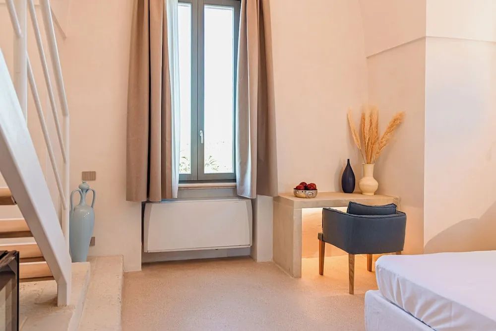 Schreibplatz mit blauem Sessel neben einem Fenster mit beigen Vorhängen im Zimmer.