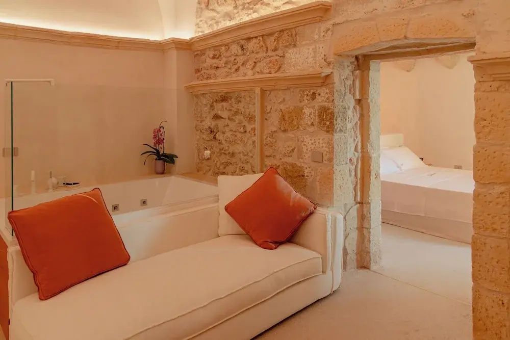 Ein Zimmer mit Sofa, Badewanne und Blick auf ein Bett im angrenzenden Raum.