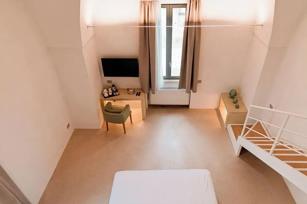 Blick von oben auf ein minimalistisches Zimmer mit Doppelbett, Schreibtisch und Fernseher.