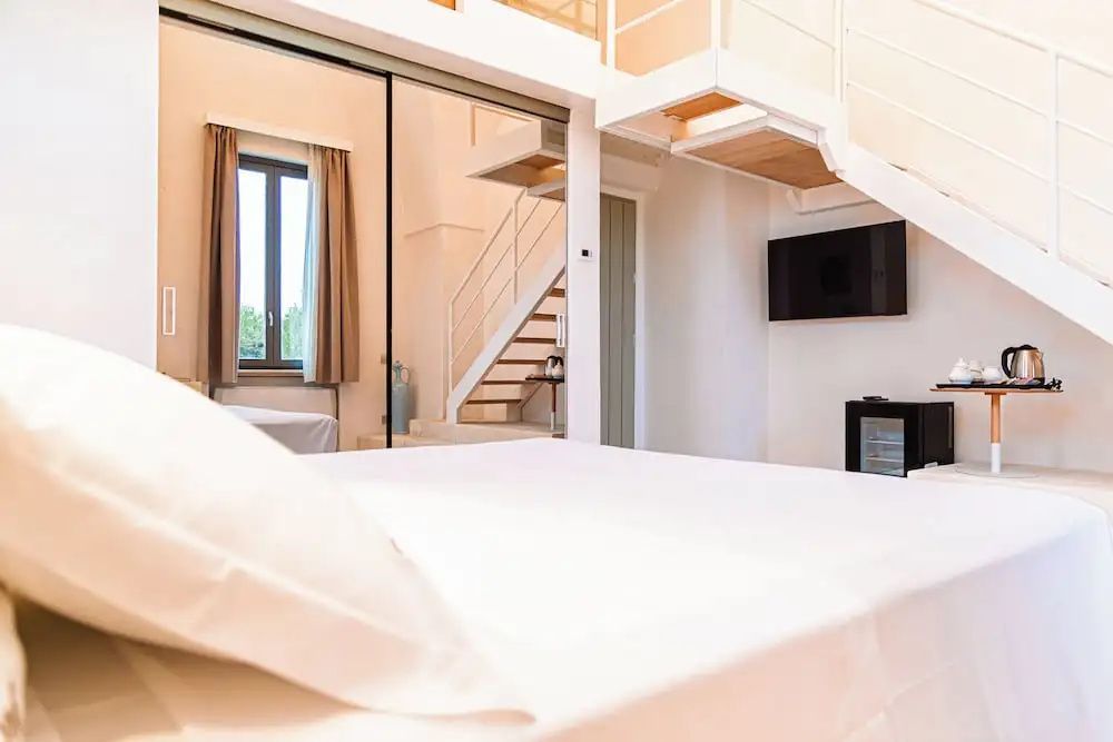 Hell eingerichtetes Hotelzimmer mit einem Doppelbett im Vordergrund und Treppe zum Schlafbereich.