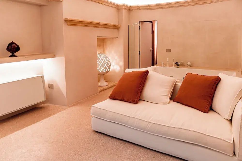 Helles Sofa mit orangefarbenen Kissen in einem mediterran gestalteten Raum.