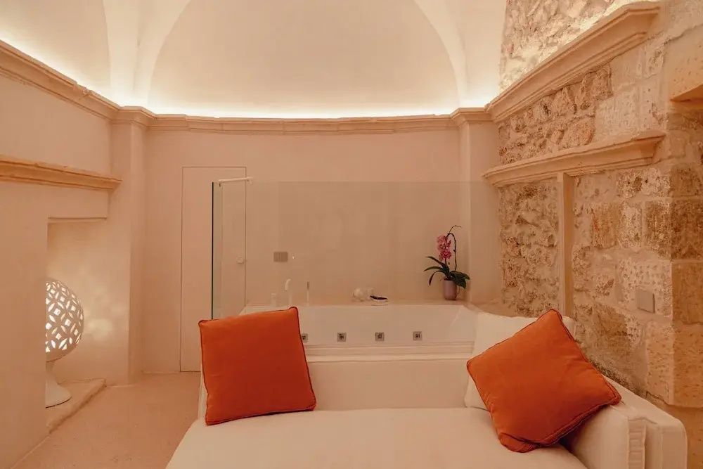 Heller Raum mit hoher Gewölbedecke, Sofa, orangefarbenen Kissen und Badewanne.