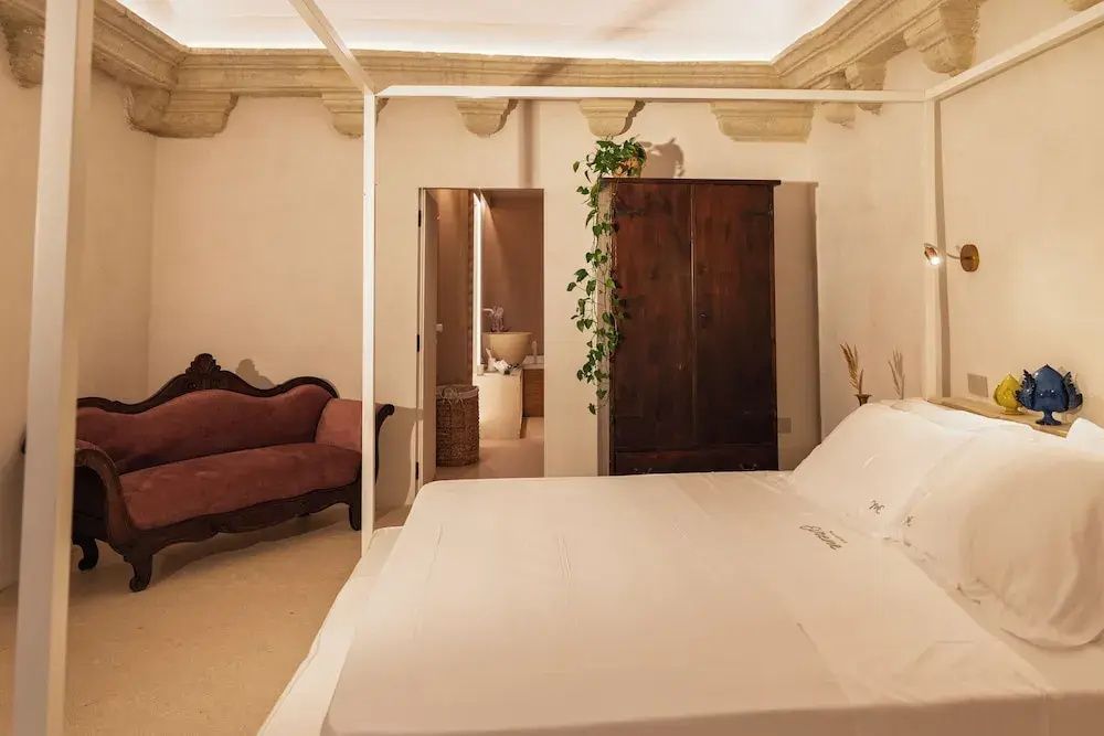 Helles Hotelzimmer mit Himmelbett, dunklem Holzschrank und antikem Sofa.