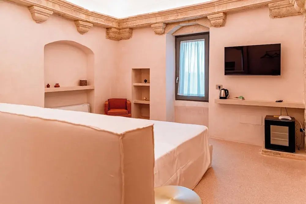Ein helles Schlafzimmer mit einem Doppelbett, Fernseher an der Wand und Fenster.
