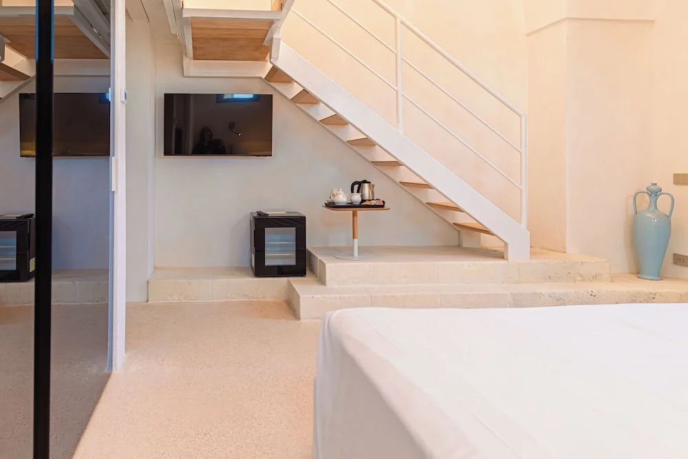Blick auf den Fernsehbereich unter der Treppe mit Minibar und Teestation im modernen Zimmer.