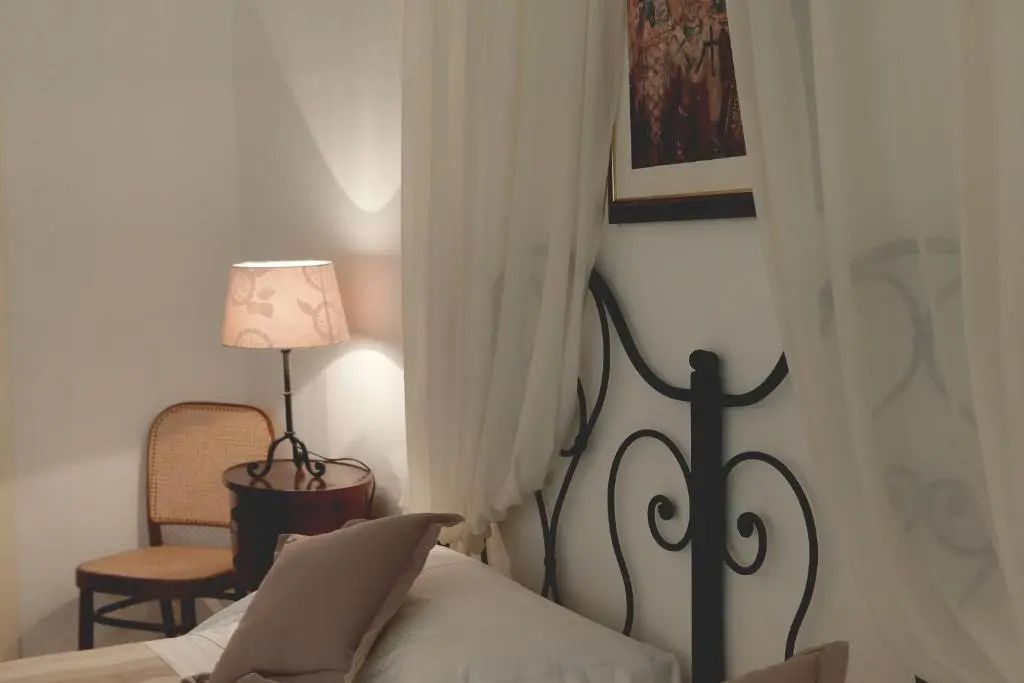 Schmiedeeisernes Bett mit weißem Vorhang, Nachttischlampe und einem Stuhl im Zimmer.