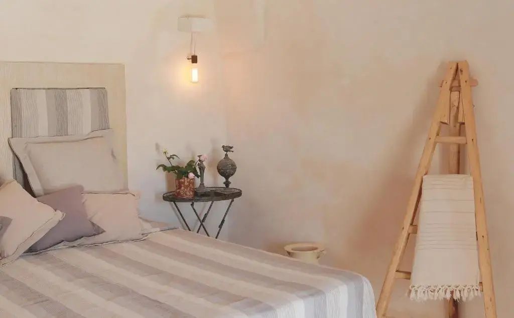 Bett mit gestreifter Tagesdecke, kleiner Beistelltisch mit Pflanze und Hängelampe an weißer Wand.