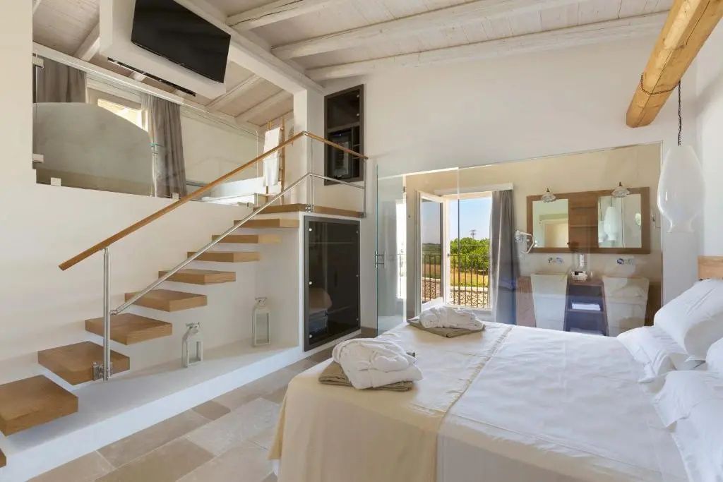 Heller Hotelraum mit Doppelbett, Holztreppe zur Empore und Glaswand zum Badezimmer.