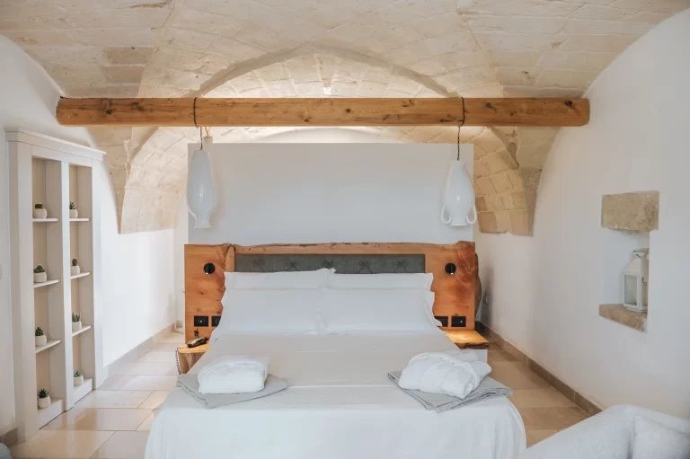 Doppelbett mit weißer Bettwäsche unter einem Natursteingewölbe mit Holzbalken.