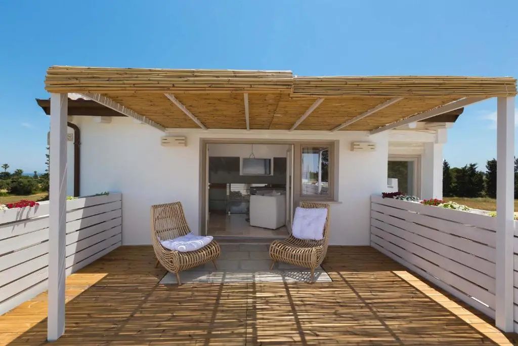 Holzterrasse mit Überdachung aus Schilf und zwei Flechtsesseln vor dem Zimmer.