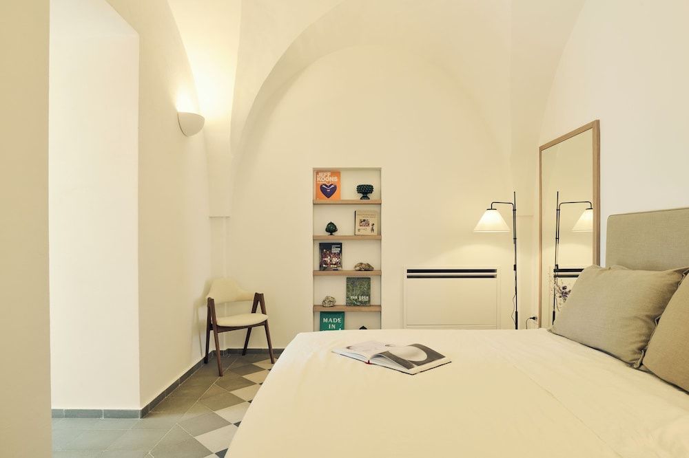 Helles Zimmer mit Gewölbedecke, einem Doppelbett, Wandregal und modernem Fliesenboden.