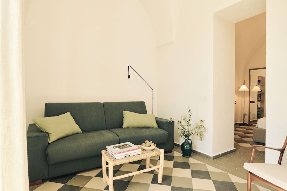 Wohnbereich mit grünem Sofa, kleinem Holztisch und zweifarbig gemustertem Fliesenboden.
