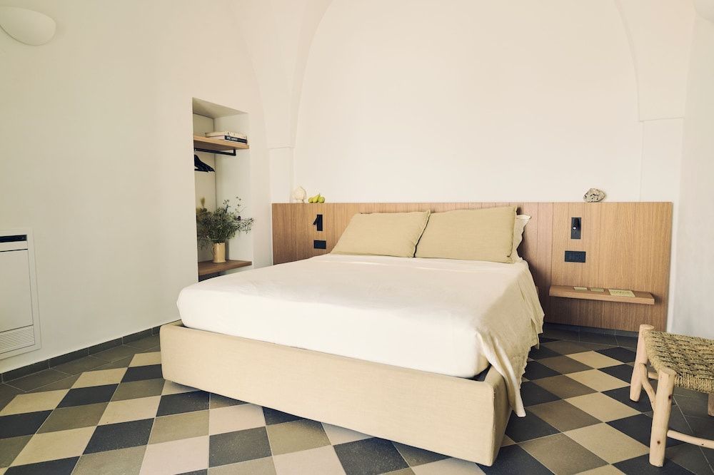 Doppelbett mit hellen Kissen und Holzkopfteil in einem hell eingerichteten Zimmer mit Musterboden.