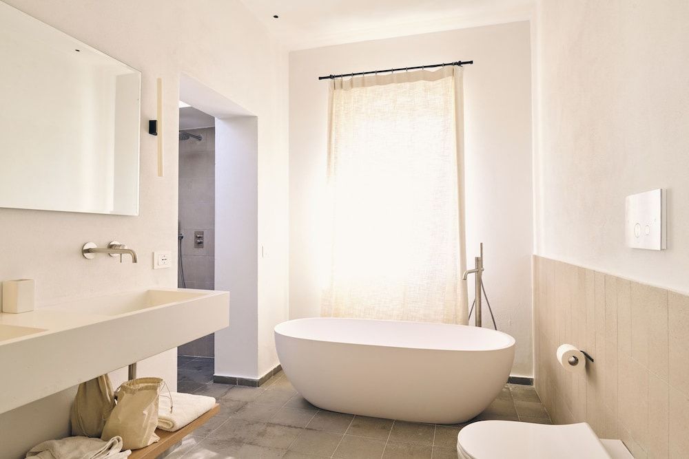 Helles Badezimmer mit Waschtisch, freistehender Badewanne und Durchgang zur Dusche.