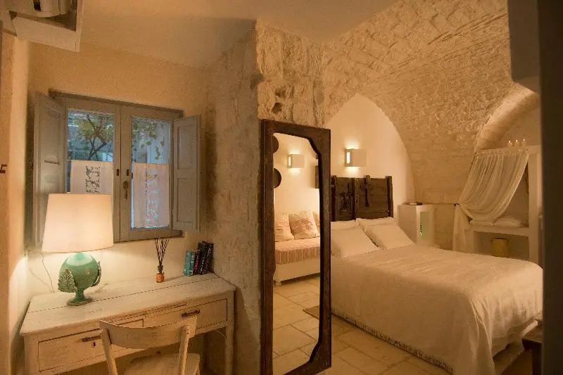 Helles Schlafzimmer mit Steinbogen, Standspiegel und einem Schreibtisch am Fenster.
