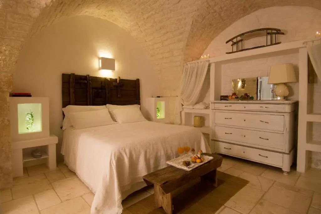 Schlafzimmer unter einer gewölbten Steindecke mit weißem Bett und Holzkommode.