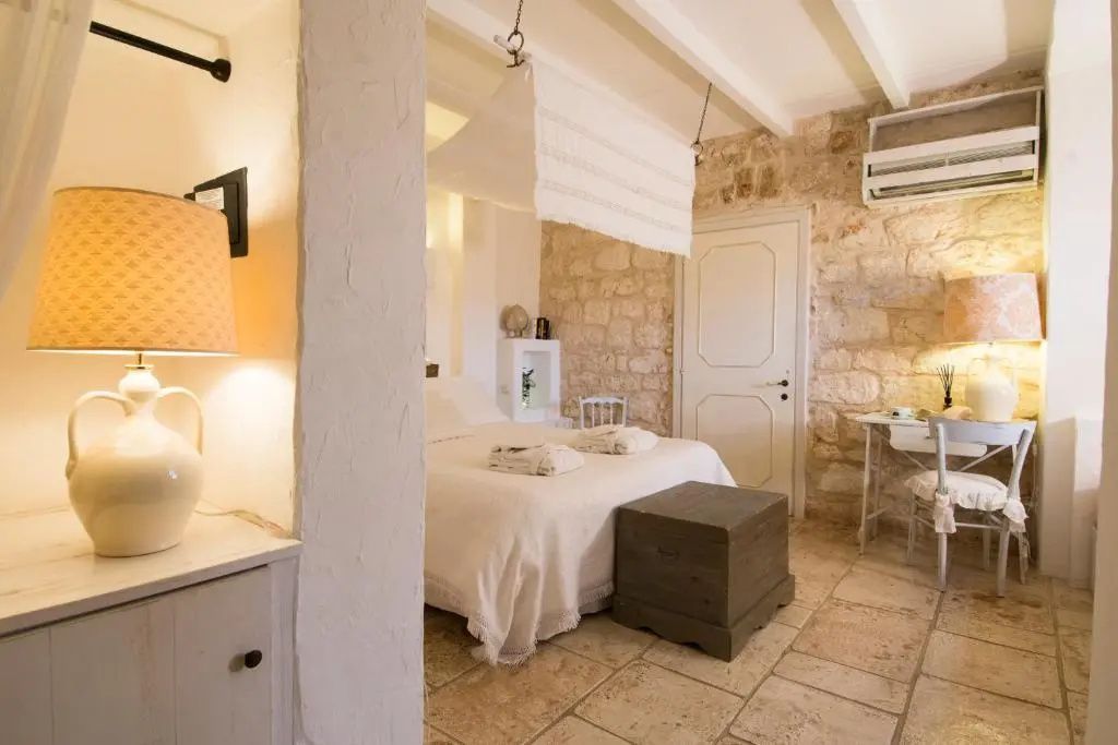 Helles Hotelzimmer mit Natursteinwänden, weißem Bett und hellen Fliesenböden.