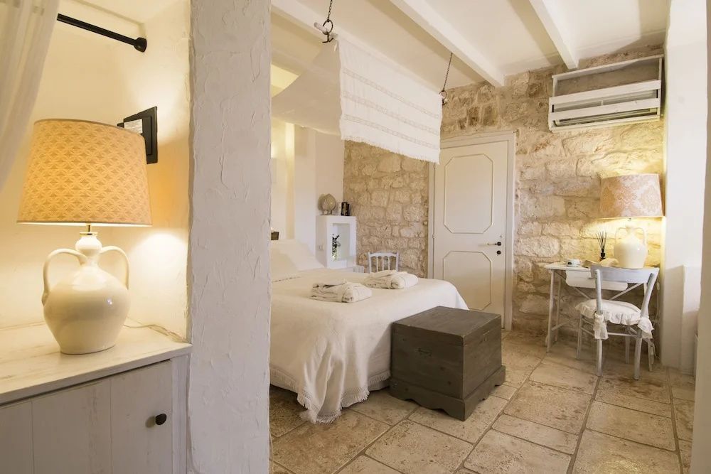 Helles Hotelzimmer mit Natursteinwand, Fliesenboden und weißem Doppelbett.