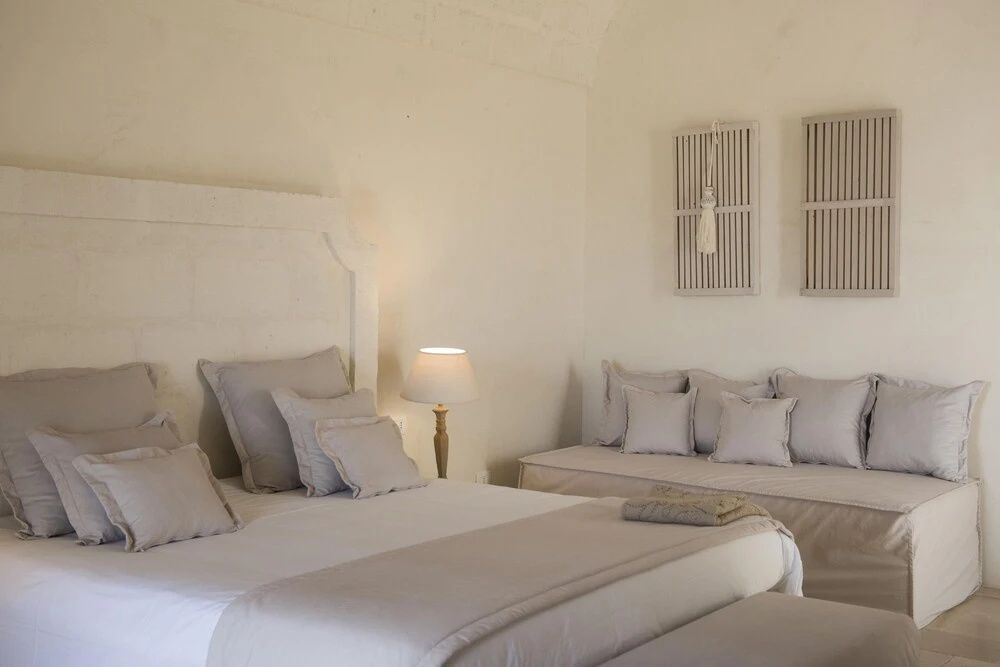 Helles Hotelzimmer in Weißtönen mit einem Doppelbett und einer Sitzbank.