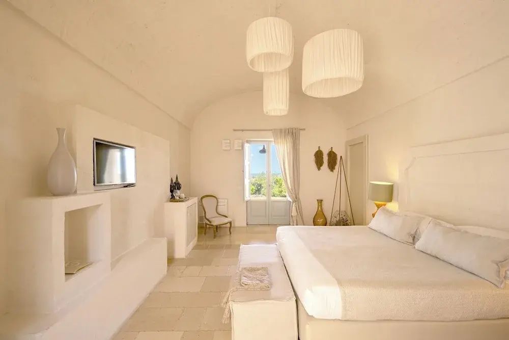 Hell eingerichtetes Hotelzimmer mit Doppelbett und Fenster ins Grüne.