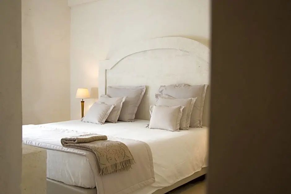 Doppelbett mit hellen Kissen und Decke in einem weiß getünchten Hotelzimmer.