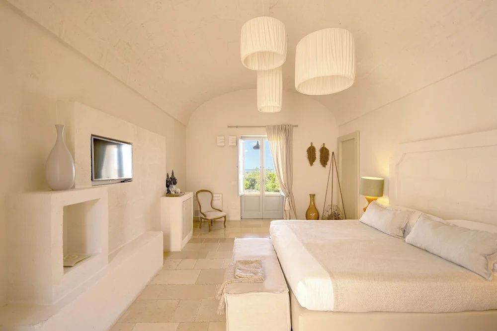 Helles Hotelzimmer mit gewölbter Decke, Doppelbett, Wand-TV und Balkontür.