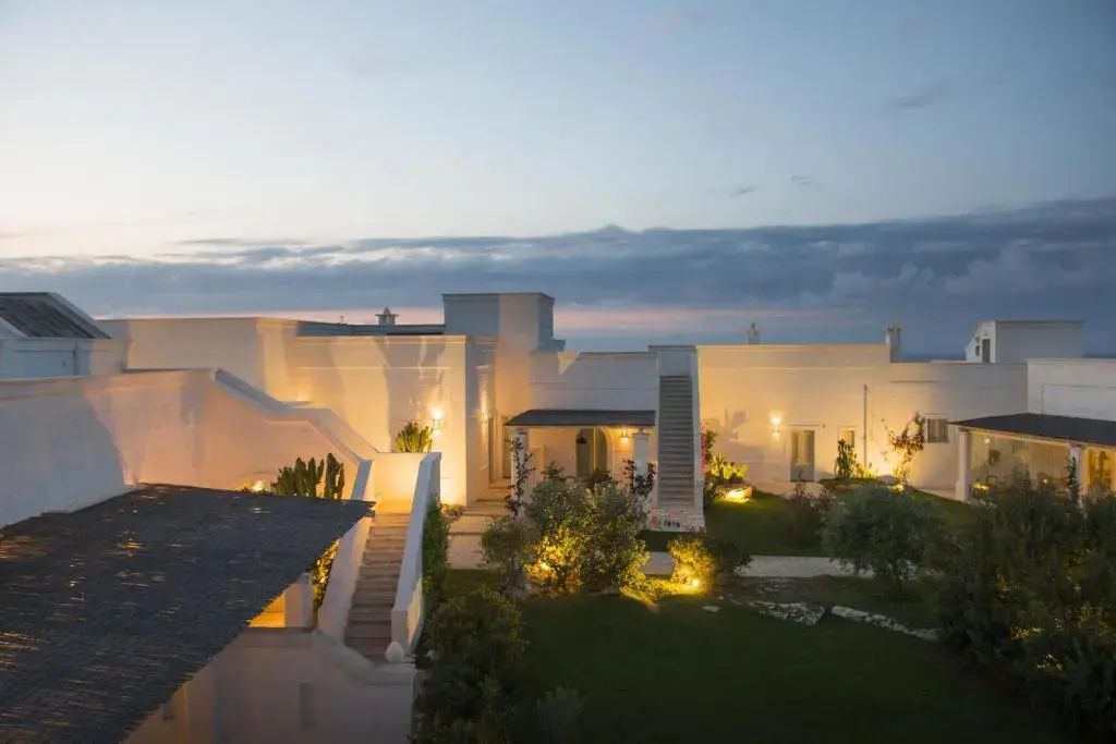 Weiß geweißtes Gebäude einer Masseria in der Dämmerung mit beleuchtetem Garten und Treppen.