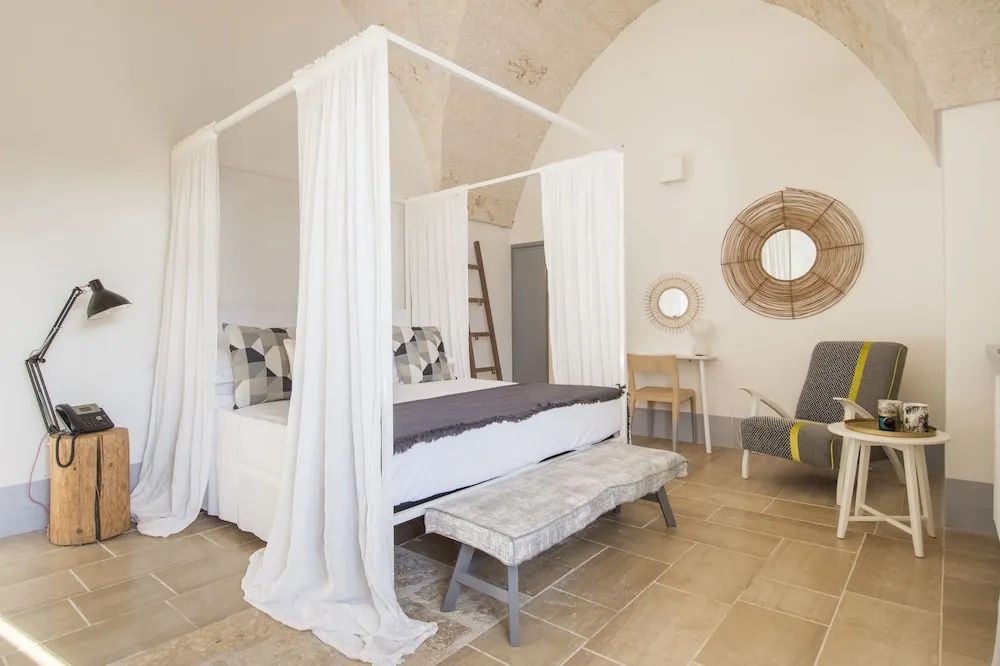 Helles Hotelzimmer mit einem weißen Himmelbett, gewölbter Decke und Fliesenboden aus Naturstein.