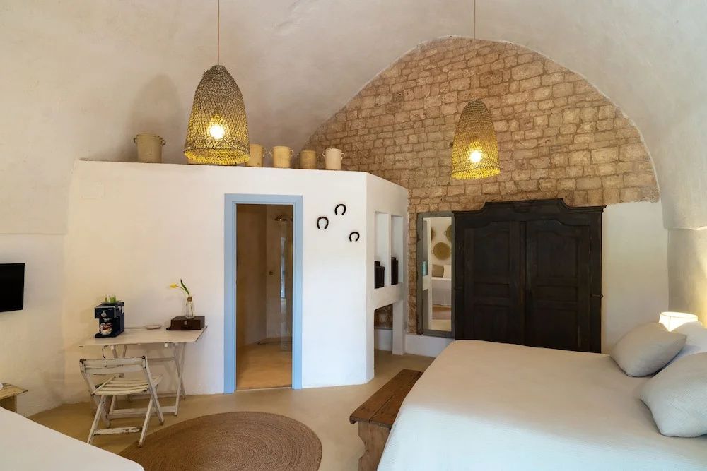 Schlafzimmer mit Natursteinwand, Holzschrank, Flechtlampen und Blick ins Bad.